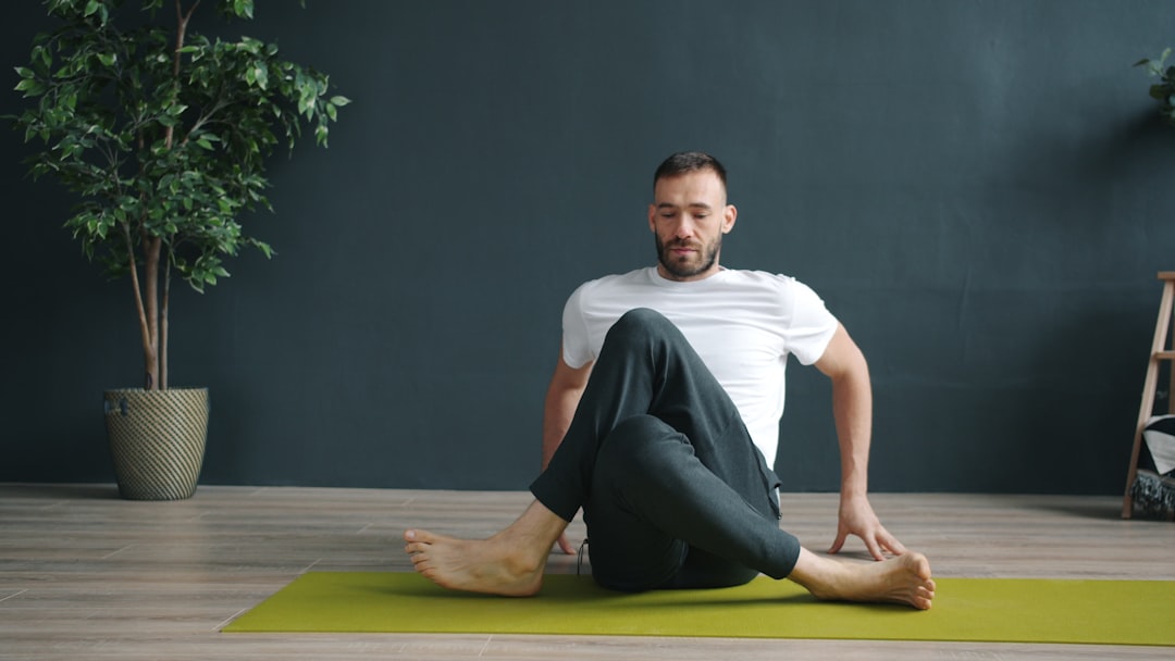 Man in white shirt twists body on yoga mat.